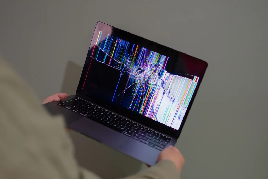 aptop with a cracked and distorted display showing colourful lines, illustrating a laptop screen glitch or hardware display problem.