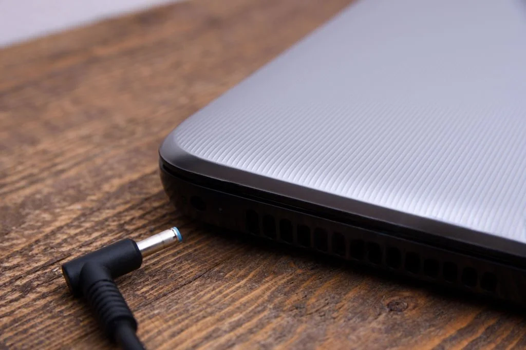 Close-up of a laptop charger connector placed near a laptop charging port, illustrating a situation where a laptop charging port is not working or a loose connection prevents the laptop from charging.
