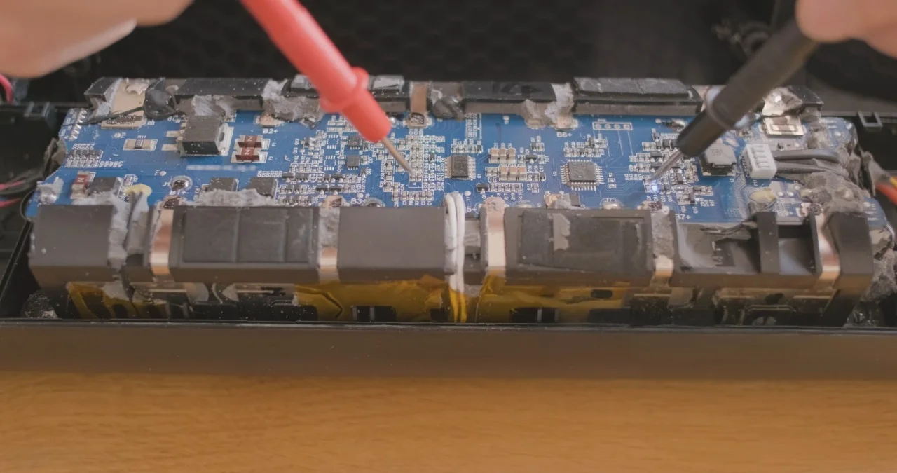 Close-up of a laptop circuit board being tested with multimeter probes while diagnosing a laptop charging port not working issue and checking components for laptop charging port repair.