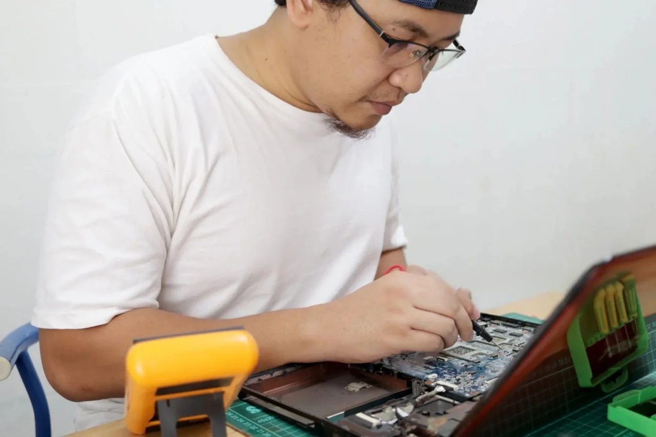 Computer repair technician working on an open laptop motherboard while diagnosing why a laptop charging port is not working and performing laptop charging port repair.