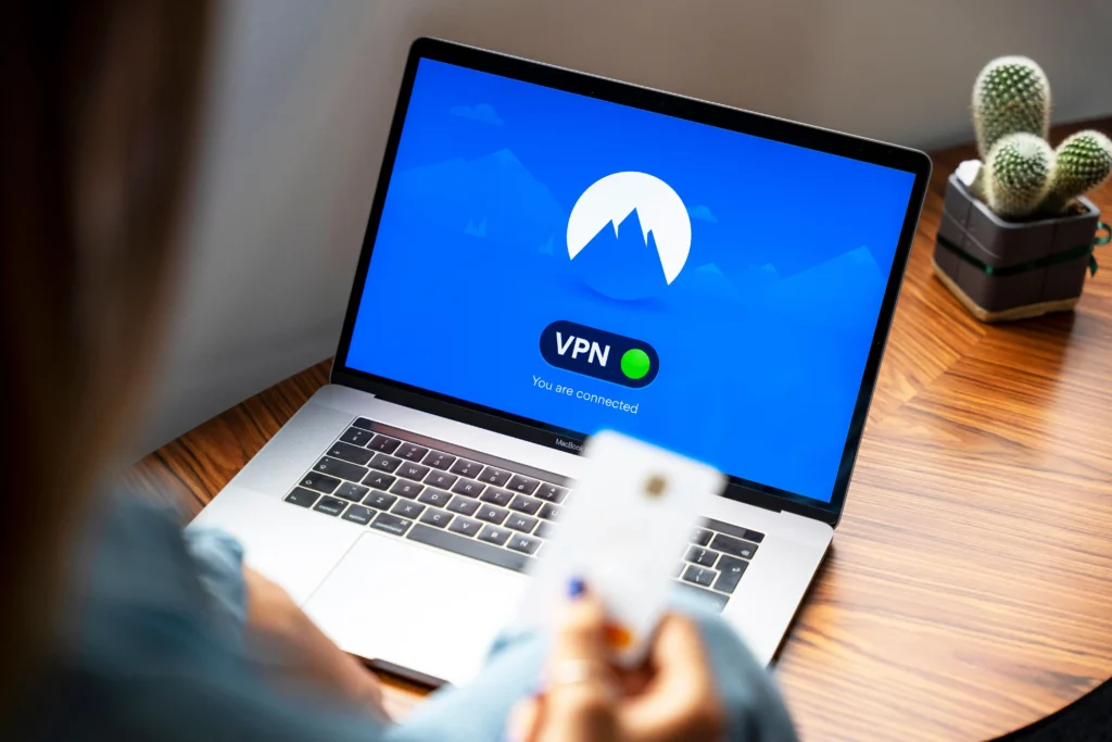 Person using a laptop with a VPN connection active, shown by a green connected indicator on the screen, while working from a wooden desk.
