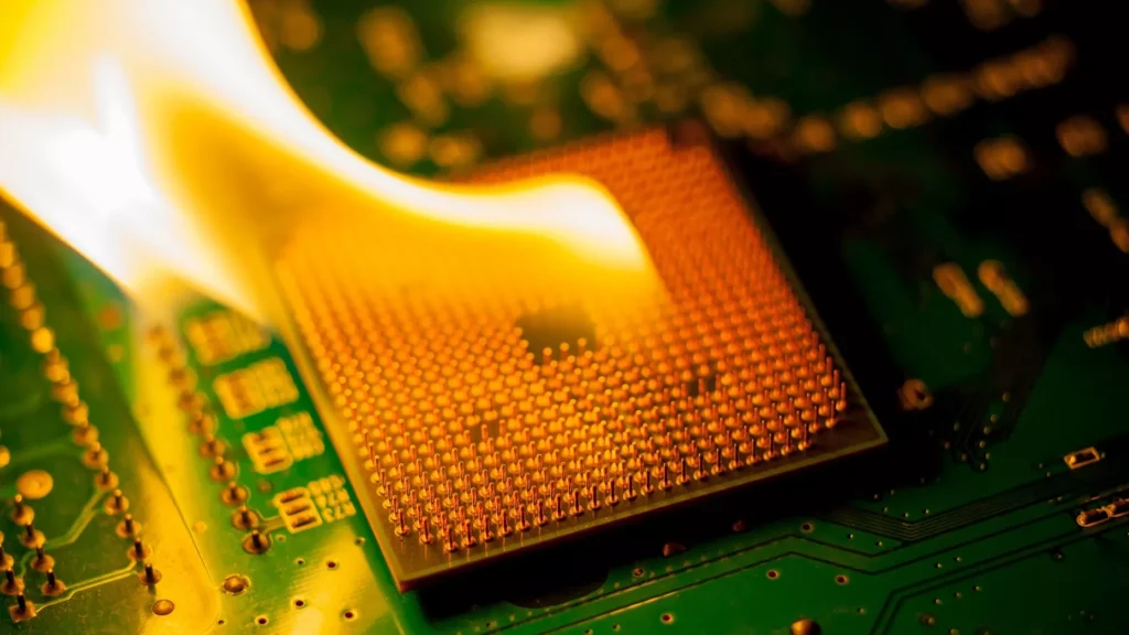 Close-up of a computer chip on a green circuit board covered in flames, symbolizing overheating