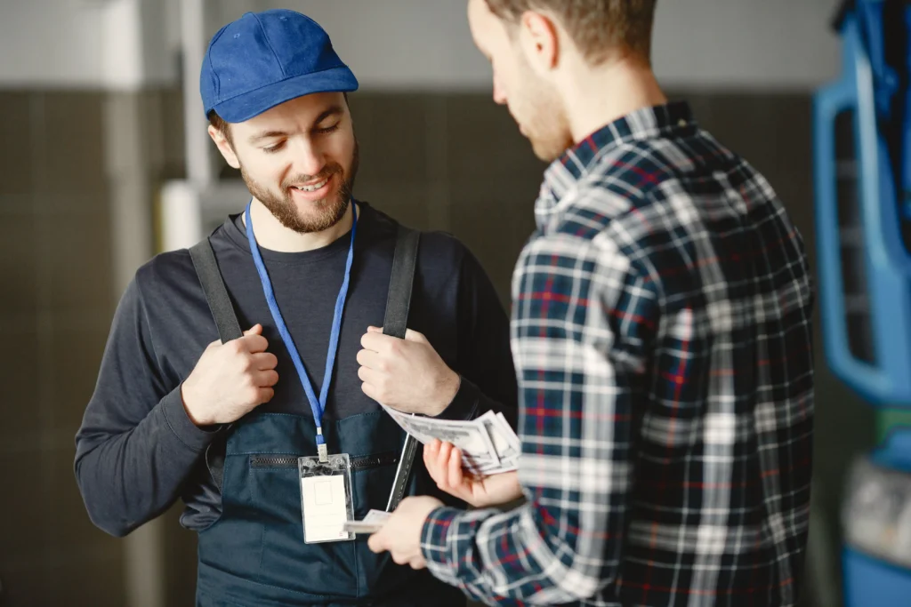 Two people discussing a laptop repair payment, with a laptop repair technician holding a tablet while a customer hands over cash, representing the cost of repairing or replacing a laptop.