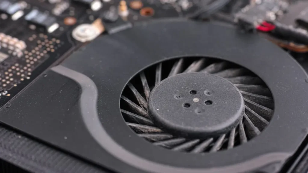 Close-up of a dusty computer cooling fan on a motherboard. The fan's blades are covered in dust, highlighting lack of maintenance and tech wear.