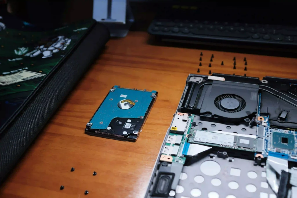 Disassembled laptop resting on a wooden desk alongside an extracted 2.5-inch hard drive.