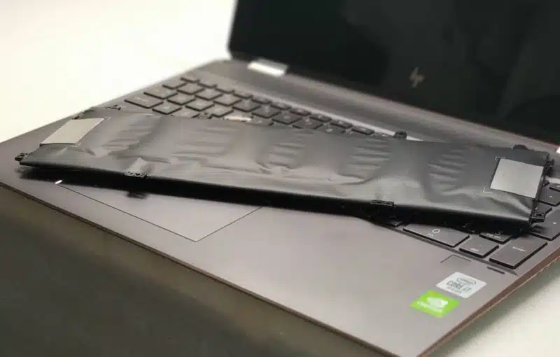 Swollen lithium-ion laptop battery removed and resting across a laptop keyboard.